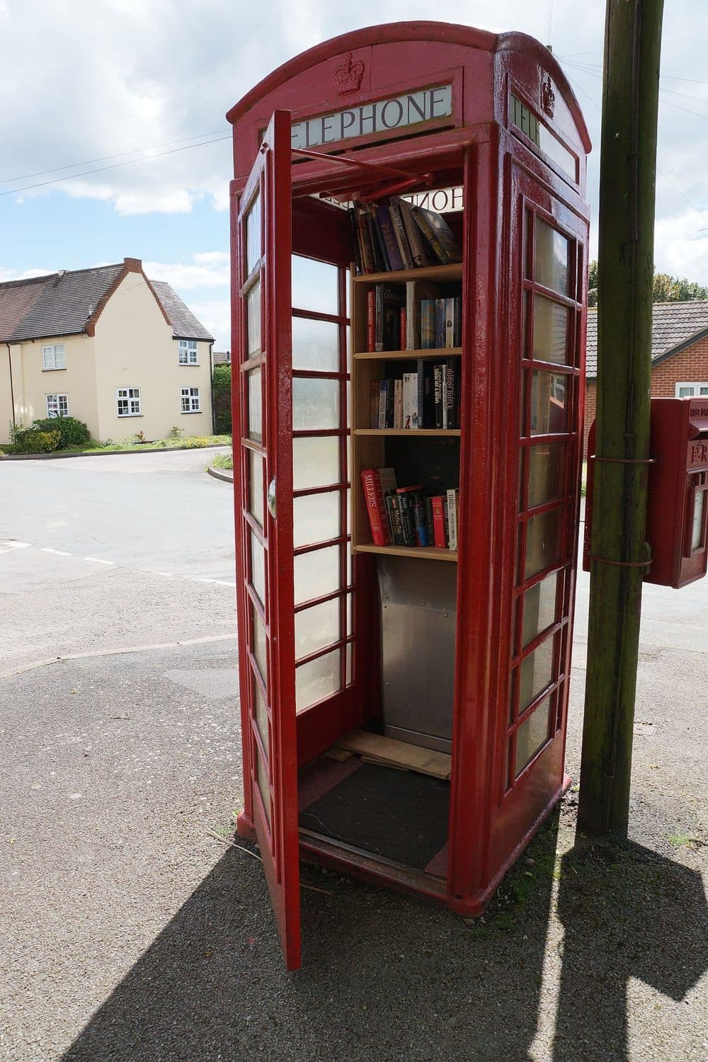 Una cabina telefonica rossa con la porta aperta e gli scaffali di libri all’interno