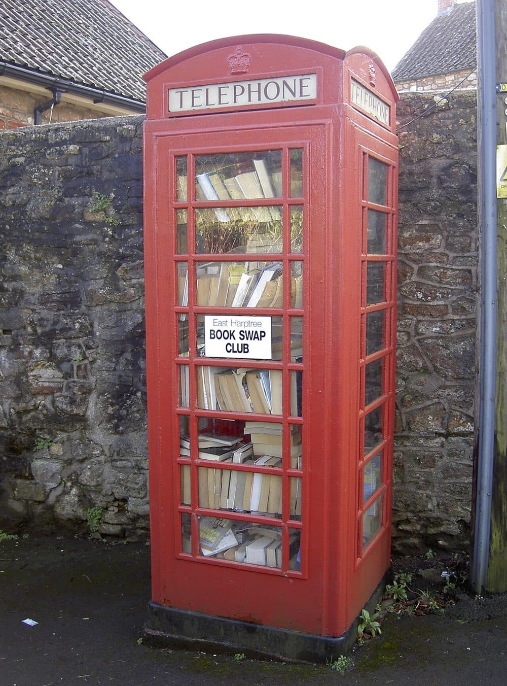 Una cabina telefonica rossa piena di libri, con un cartello «Book swap club»